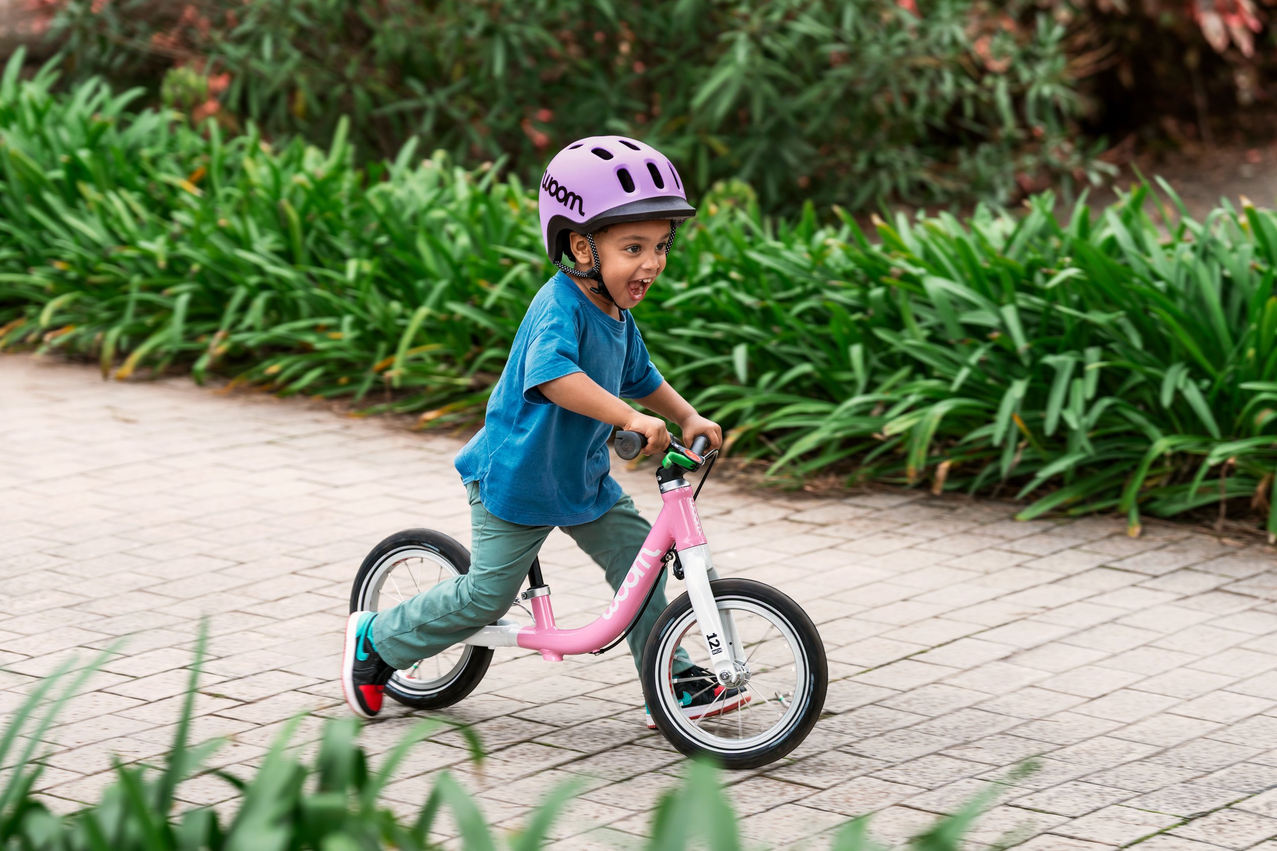 Un petit portant un casque READY se tient sur une draisienne woom GO 1 rouge à côté d’un enfant sur un woom GO 4 turquoise