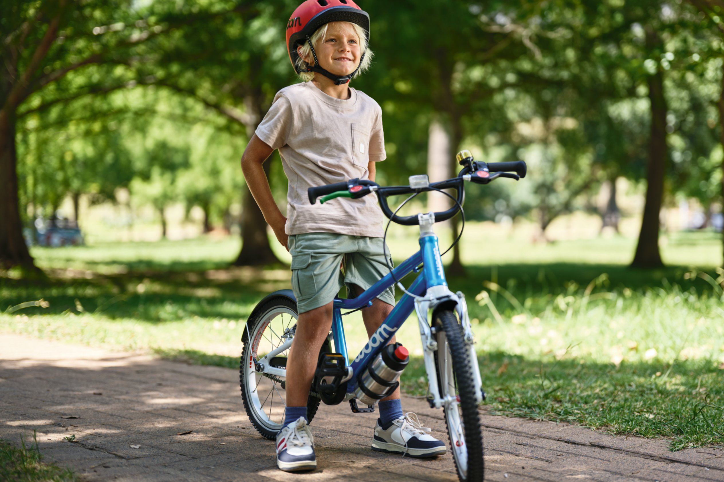 Auf dem Sattel eines blauen woom GO 3 Fahrrads sitzt ein Junge mit rotem READY Kinderhelm auf dem Kopf.