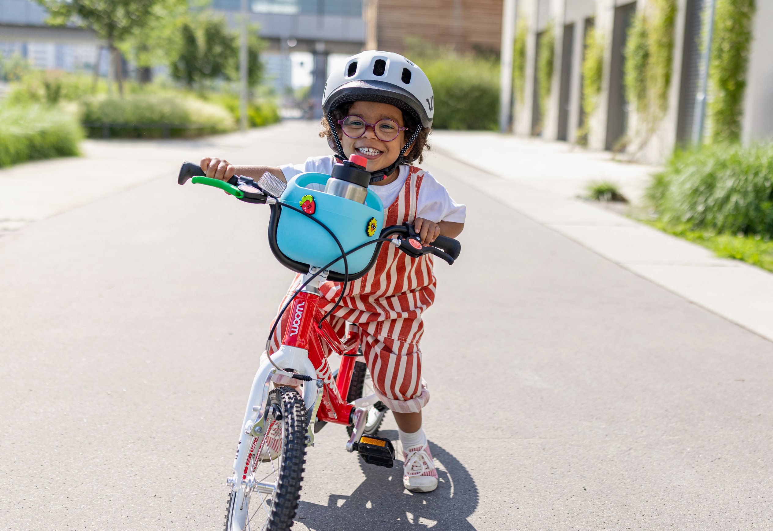 Child riding a green woom GO has the POP Kids' Bike Basket on their handlebars decorated with fun POP ONS Bike Charms