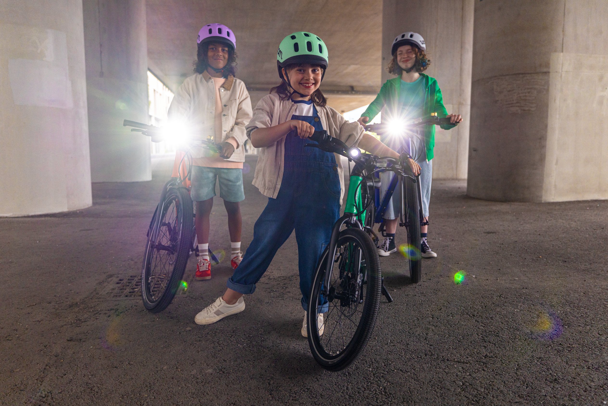 Drei Kinder stehen neben woom bikes, die mit woom BEAM Frontlichtern für bessere Sichtbarkeit in schlechten Lichtverhältnissen ausgestattet sind.