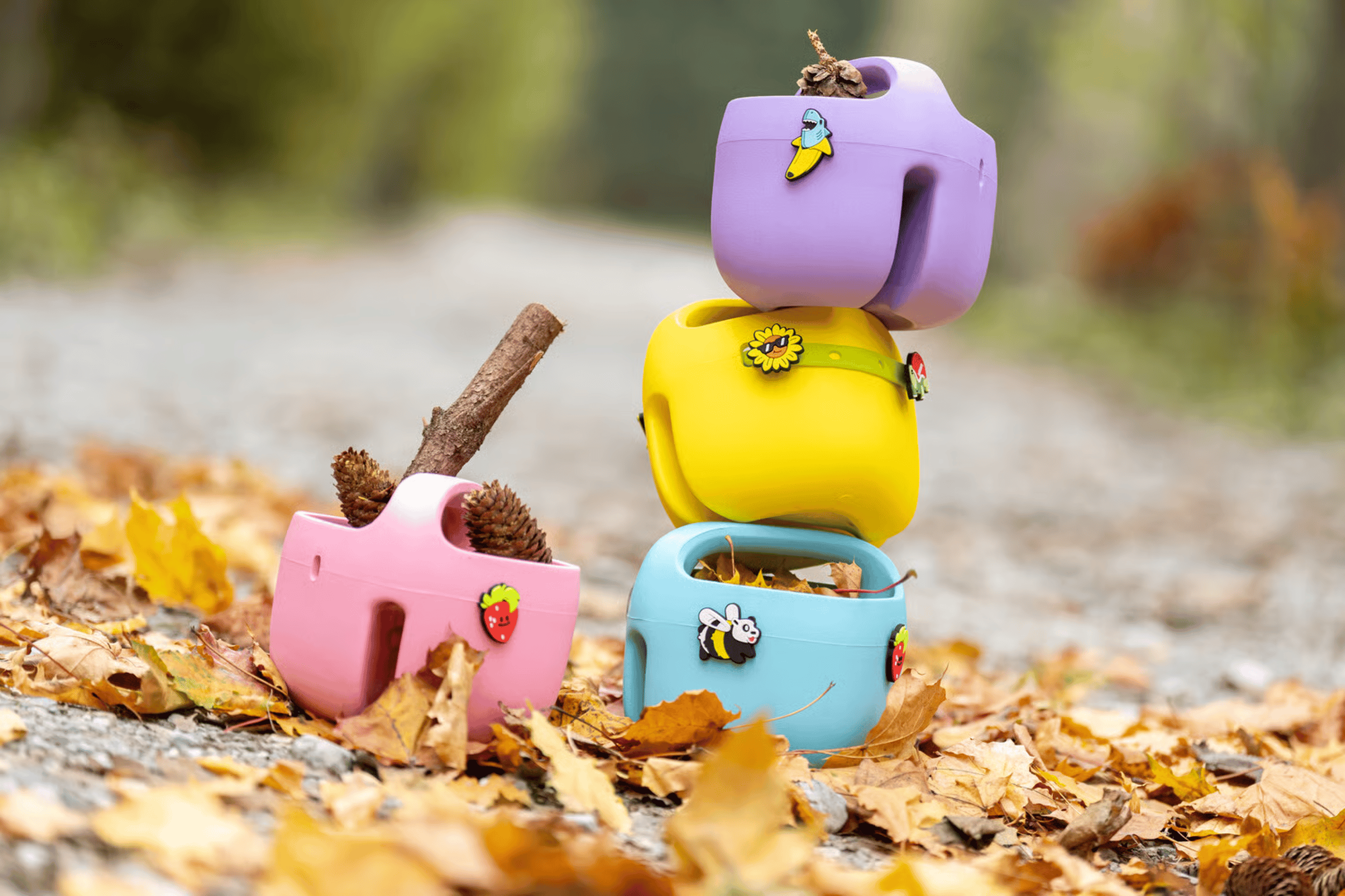 Colorful woom POP bike baskets with different POP ONS charms, stacked up in autumn leaves on a woodland path.