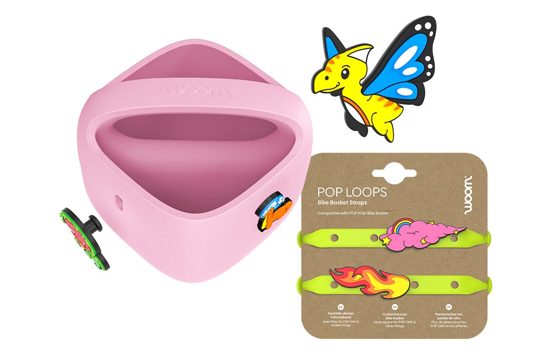 Lila woom POP Fahrradkorb mit POP ONS neben neongrünen POP LOOPS auf Karton und einem neuen Flugsaurier-POP ON darüber