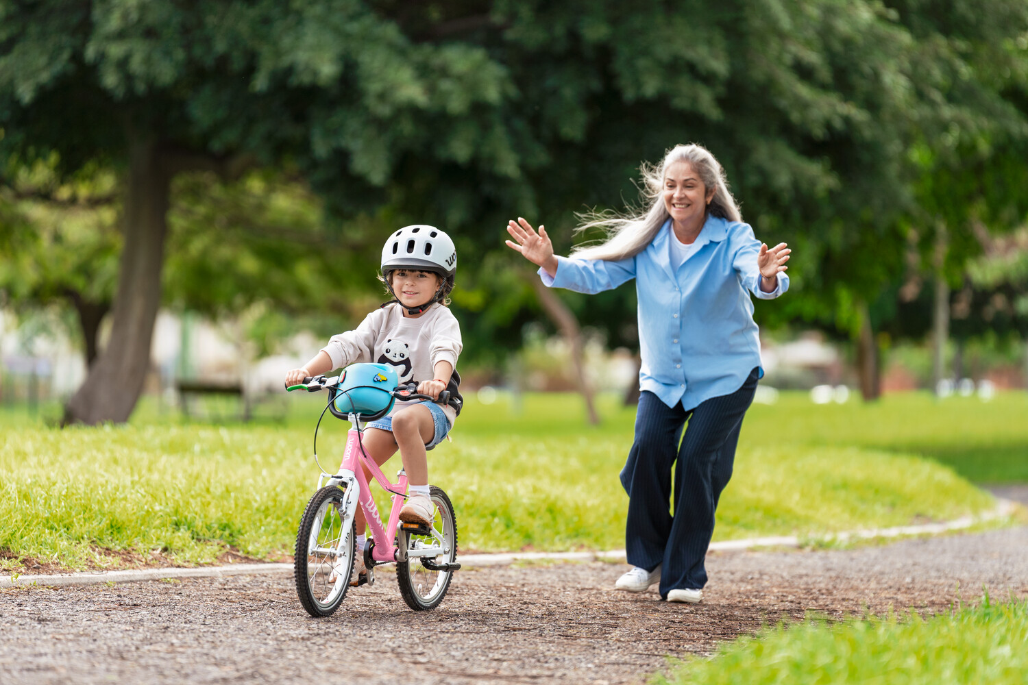 Kind mit READY Kinderhelm auf dem Kopf fährt auf dem Fahrrad woom GO 2 in der Farbe Pink. Auf dem Lenker steckt der POP Fahrradkorb in Pink.